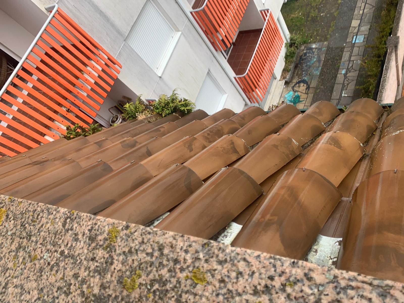 Vista inclinada de un tejado de tejas de terracota junto a paredes blancas y barandillas de balcón naranjas