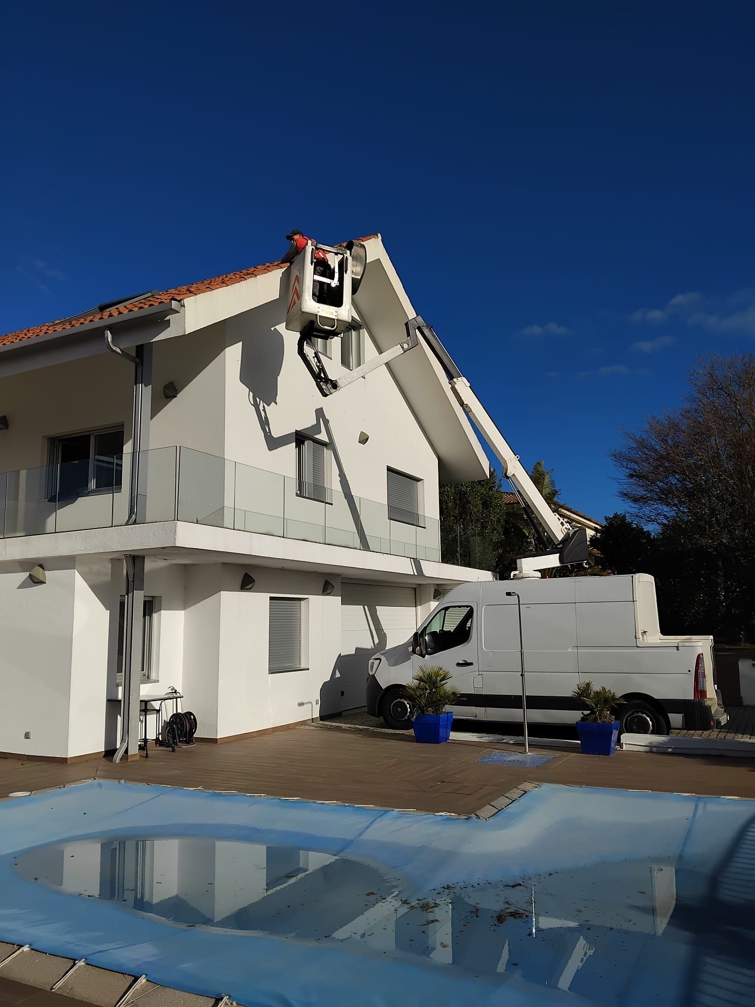 Casa blanca dañada con el techo roto sobre una piscina en el patio trasero bajo un cielo azul claro.