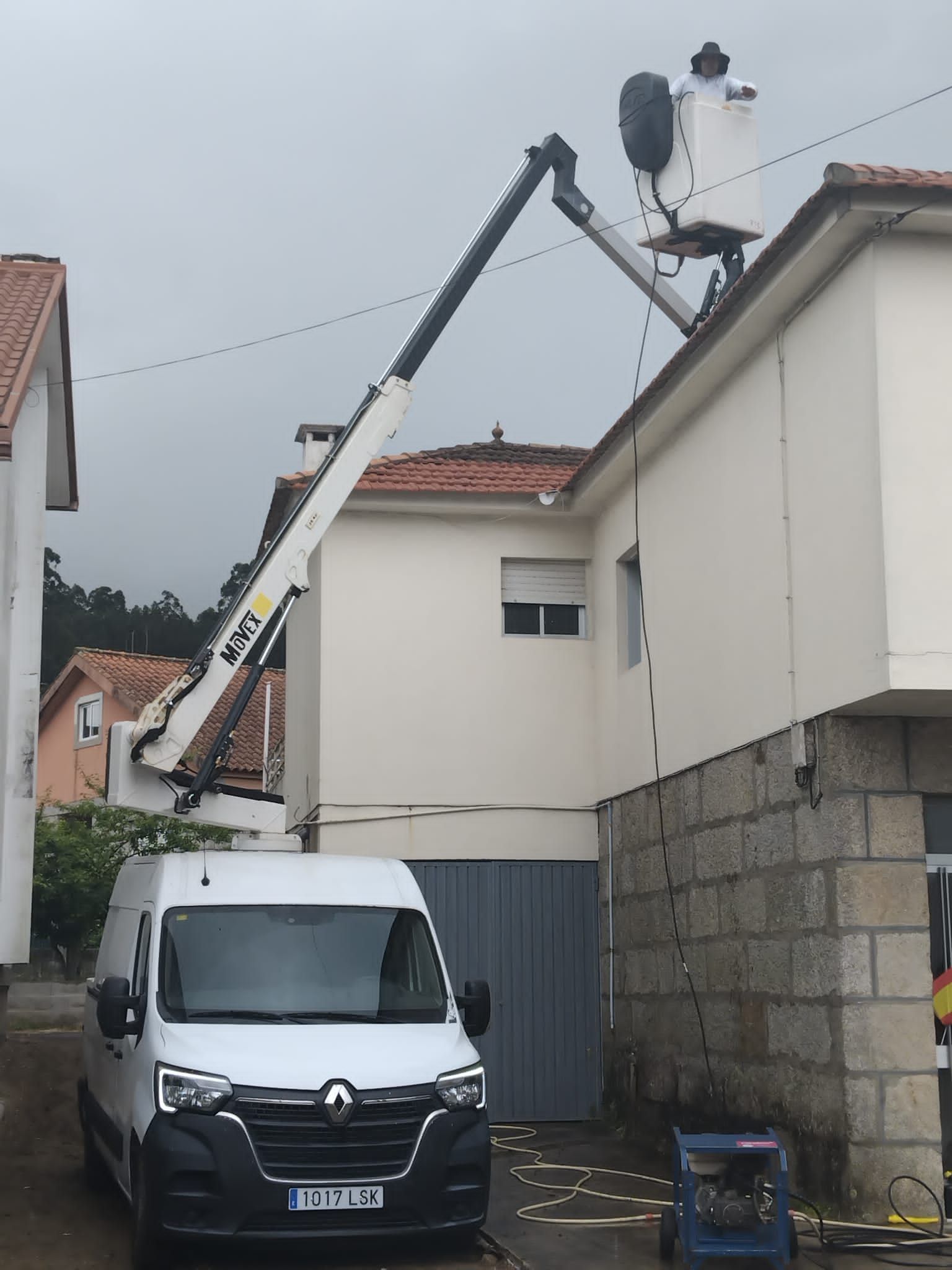 Una grúa está elevando equipos sobre el tejado de una casa en un estrecho callejón residencial.