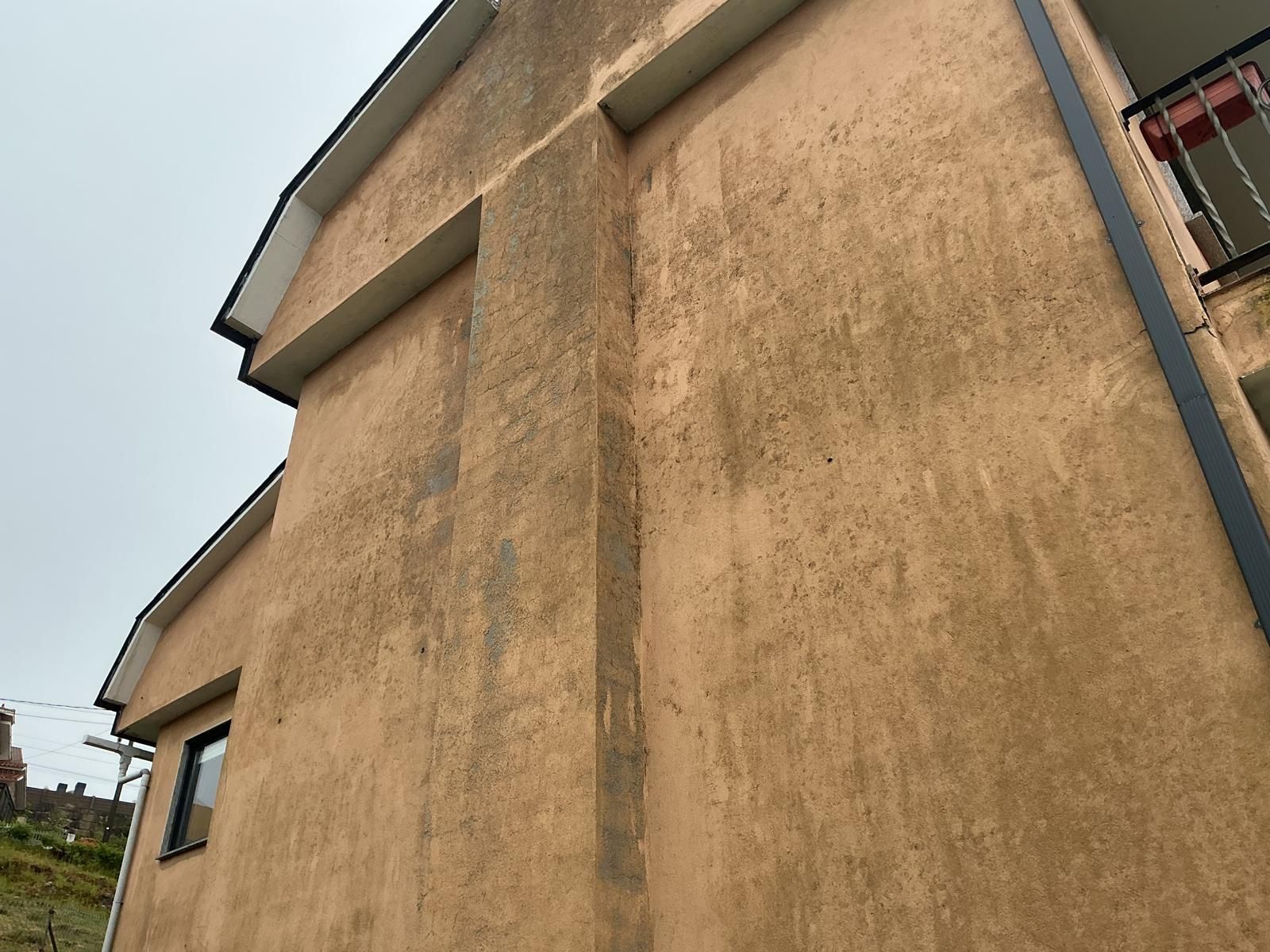 Primer plano de la pared de un edificio de estuco beige con techo inclinado y ventanas pequeñas.