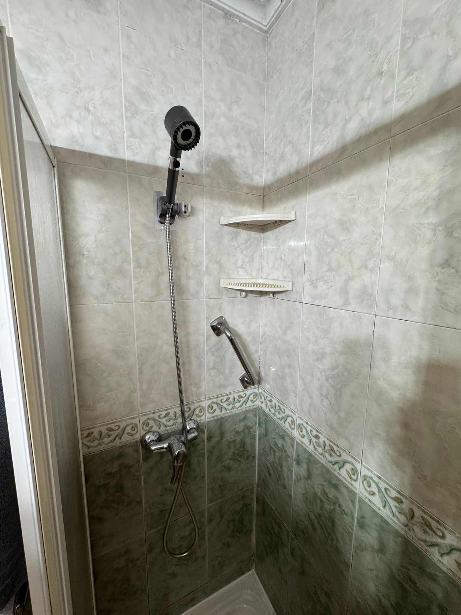 Pequeña ducha alicatada con cabezales de ducha de mano y de techo, estantes en la pared