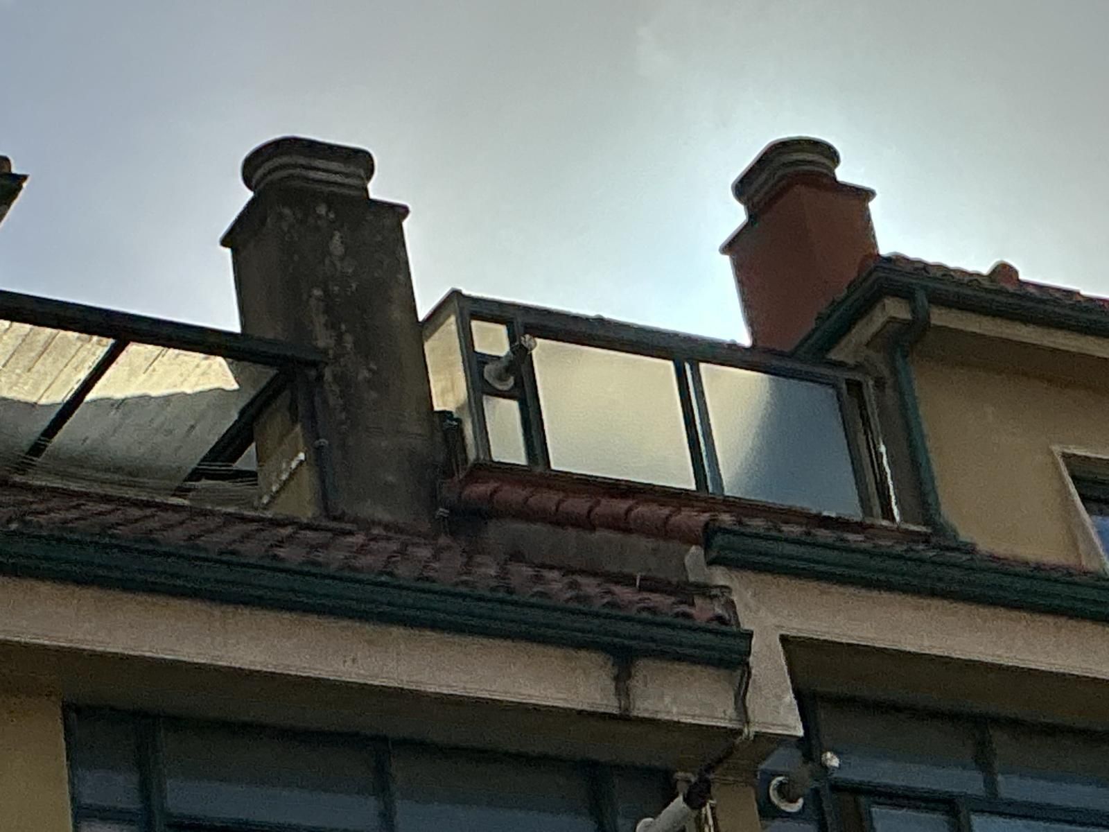 Chimeneas en el tejado y ventanas de tragaluz en una casa bajo un cielo nublado.