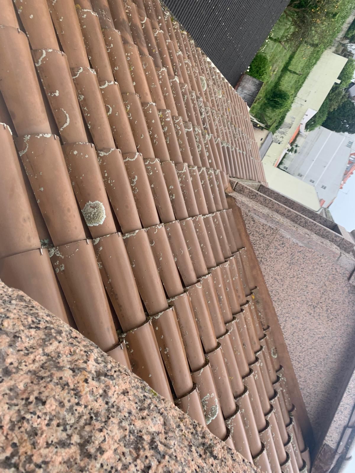 Vista inclinada de un tejado de tejas rojas con una chimenea de grava y casas vecinas cercanas.