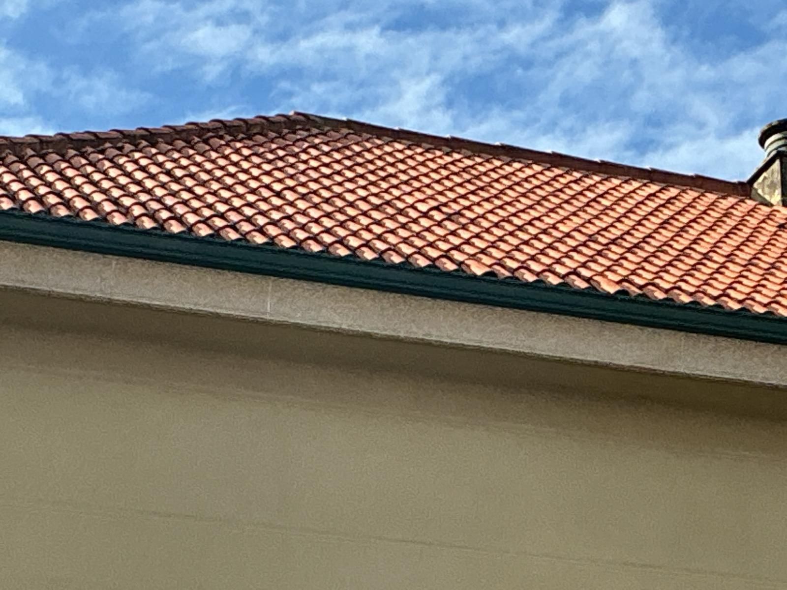 Techo de tejas rojas con pared de estuco beige bajo un cielo azul.