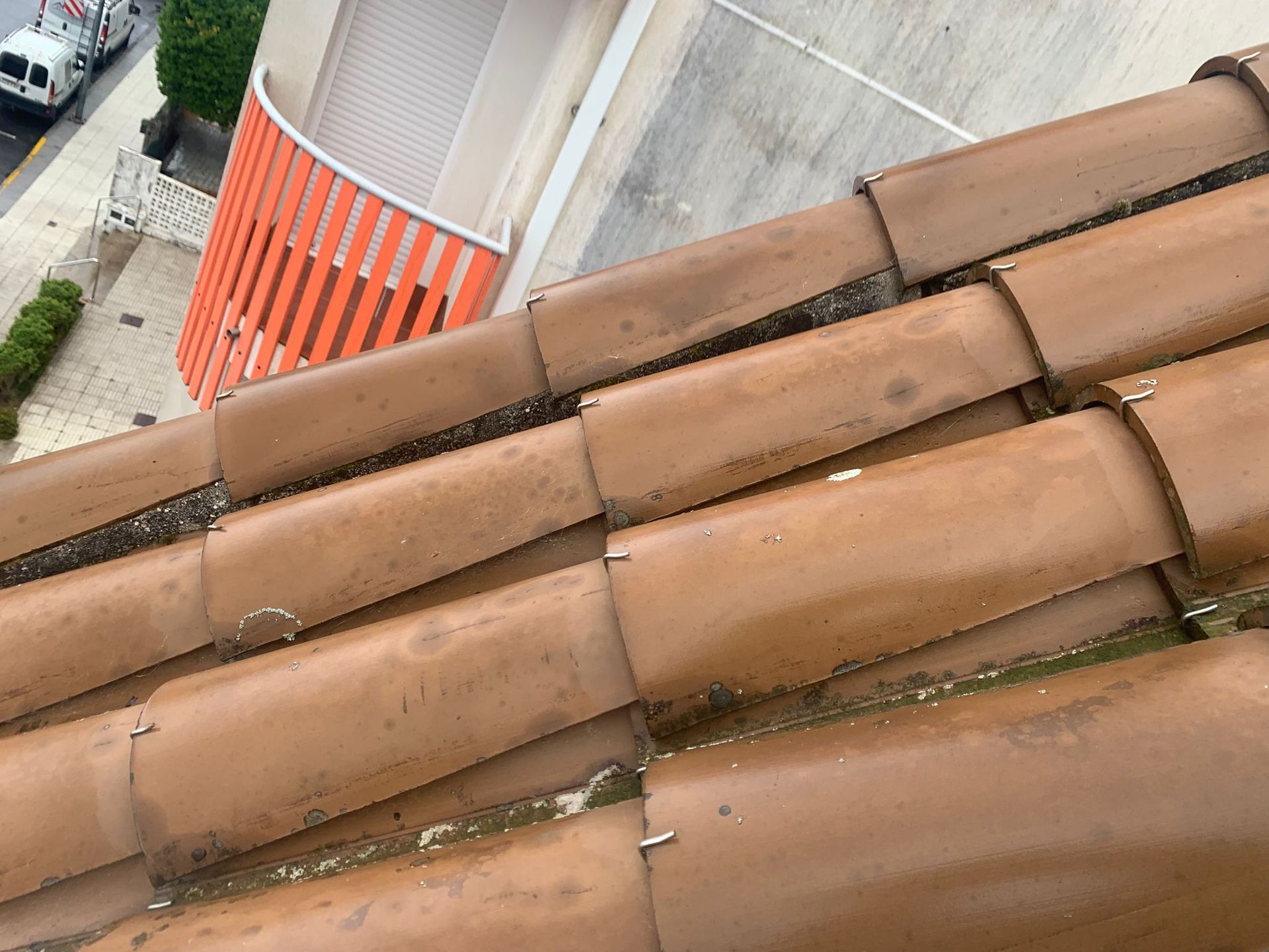 Primer plano de tejas de terracota marrón junto a un muro curvo de hormigón y un toldo a rayas naranjas.