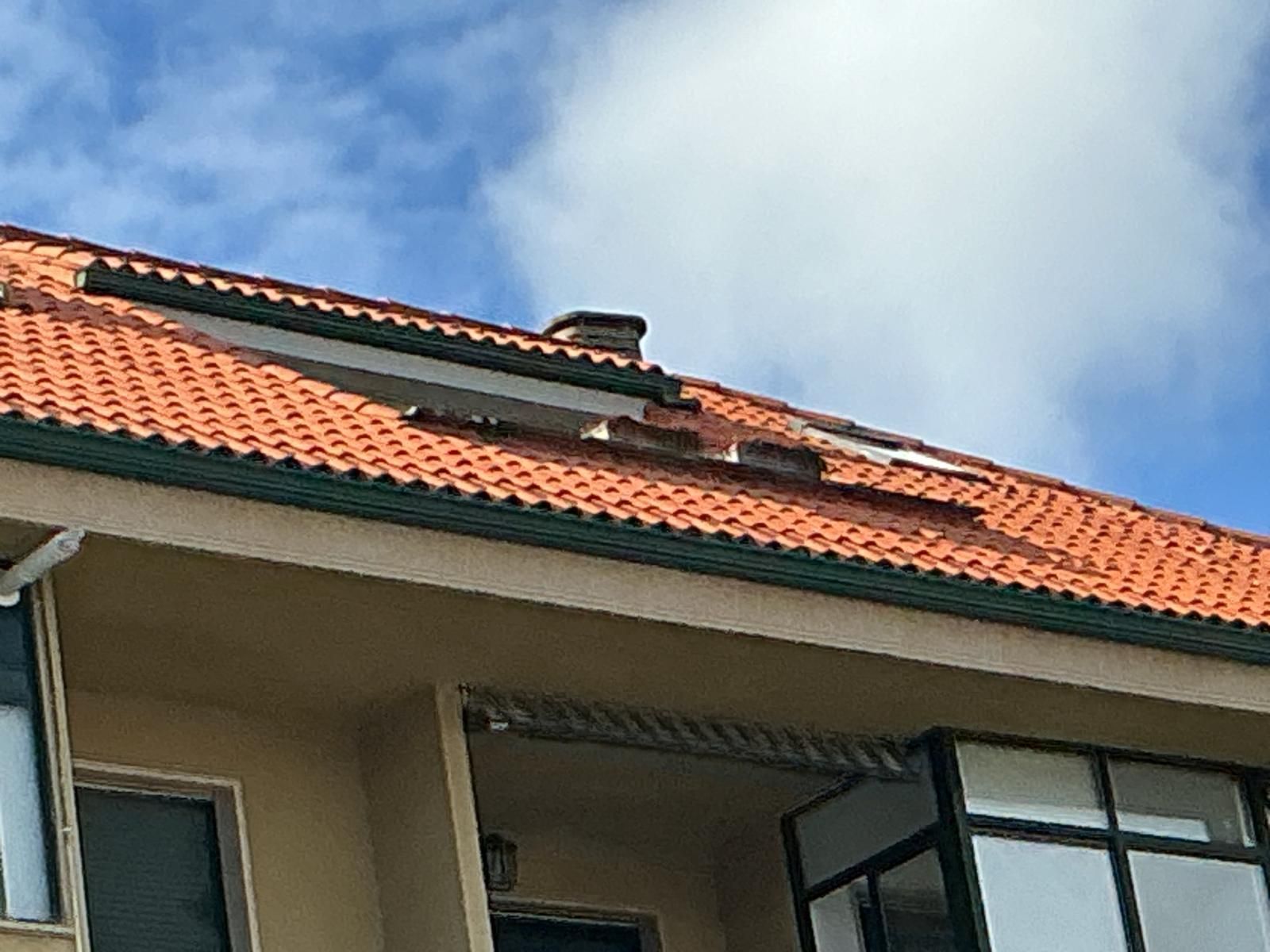 Tejado de una casa con tejas naranjas contra un cielo azul, visto desde abajo.