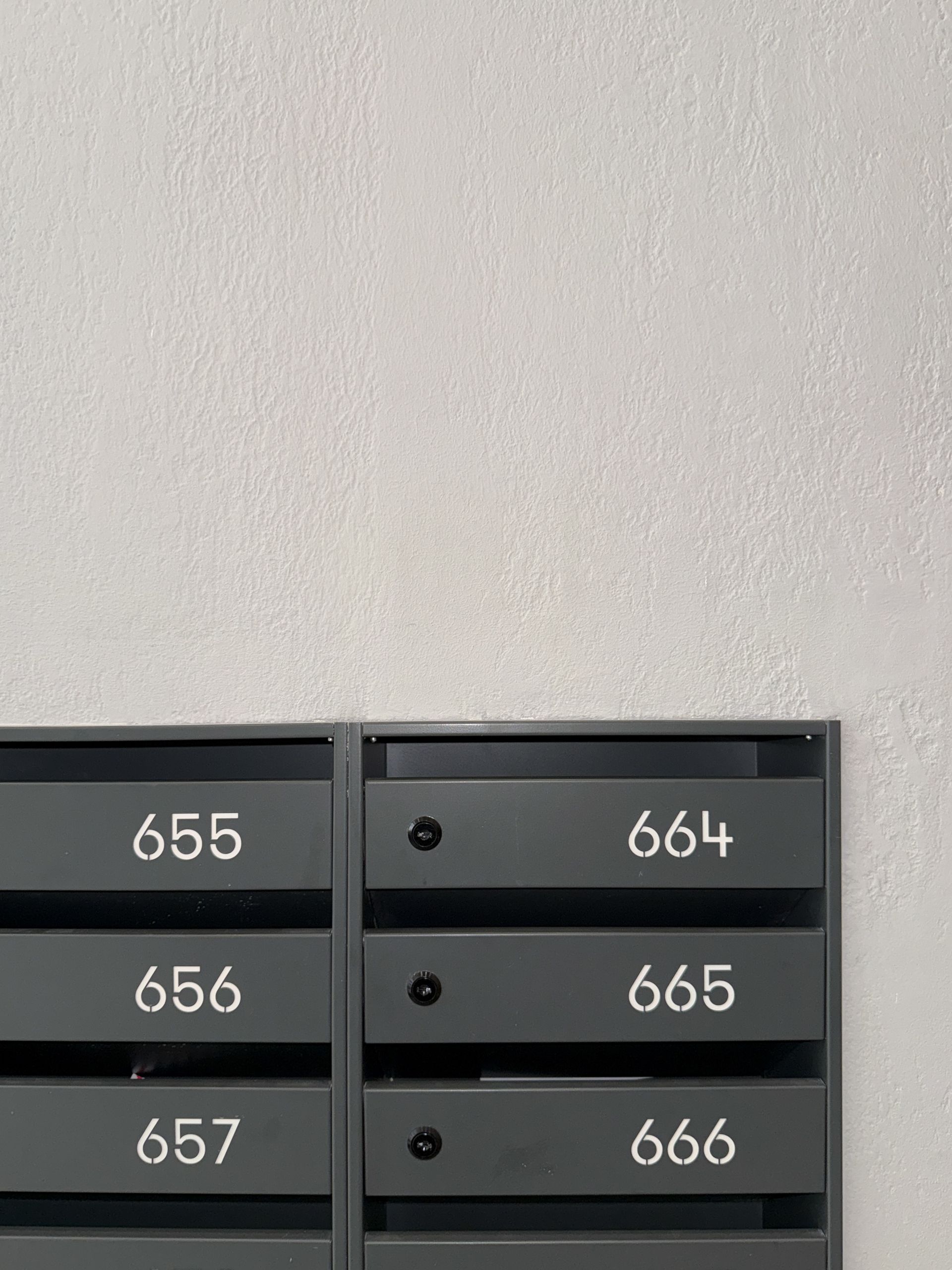 Boîtes aux lettres numérotées 655-657 et 664-666 sur un mur blanc texturé.