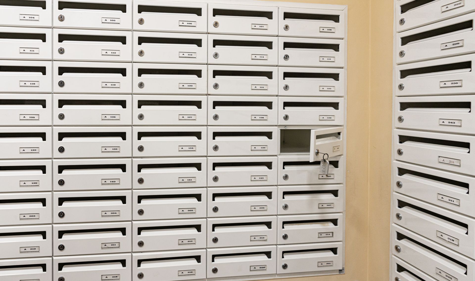 Des rangées de boîtes aux lettres en métal blanc dans le hall d'un immeuble ; une porte est ouverte avec une clé.