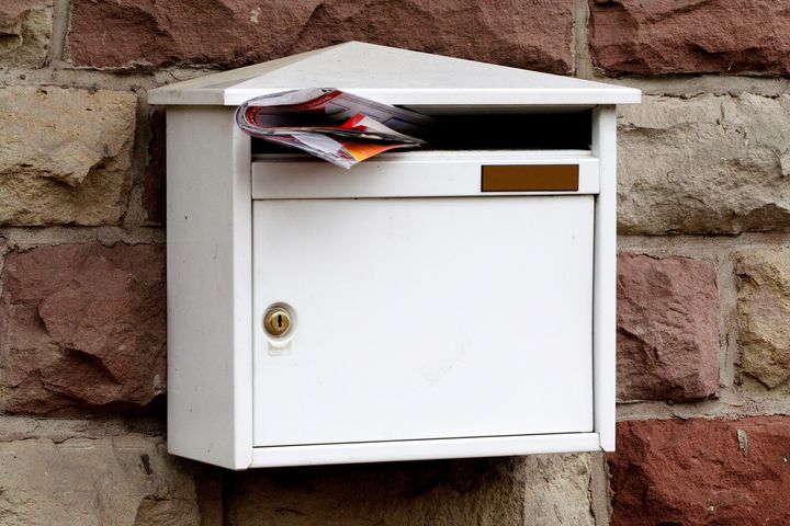 Boîte aux lettres blanche débordant de courrier, fixée sur un mur de pierre.