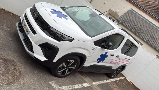 Ambulance blanche avec l'étoile bleue de vie ; garée à l'extérieur, logo VW visible.