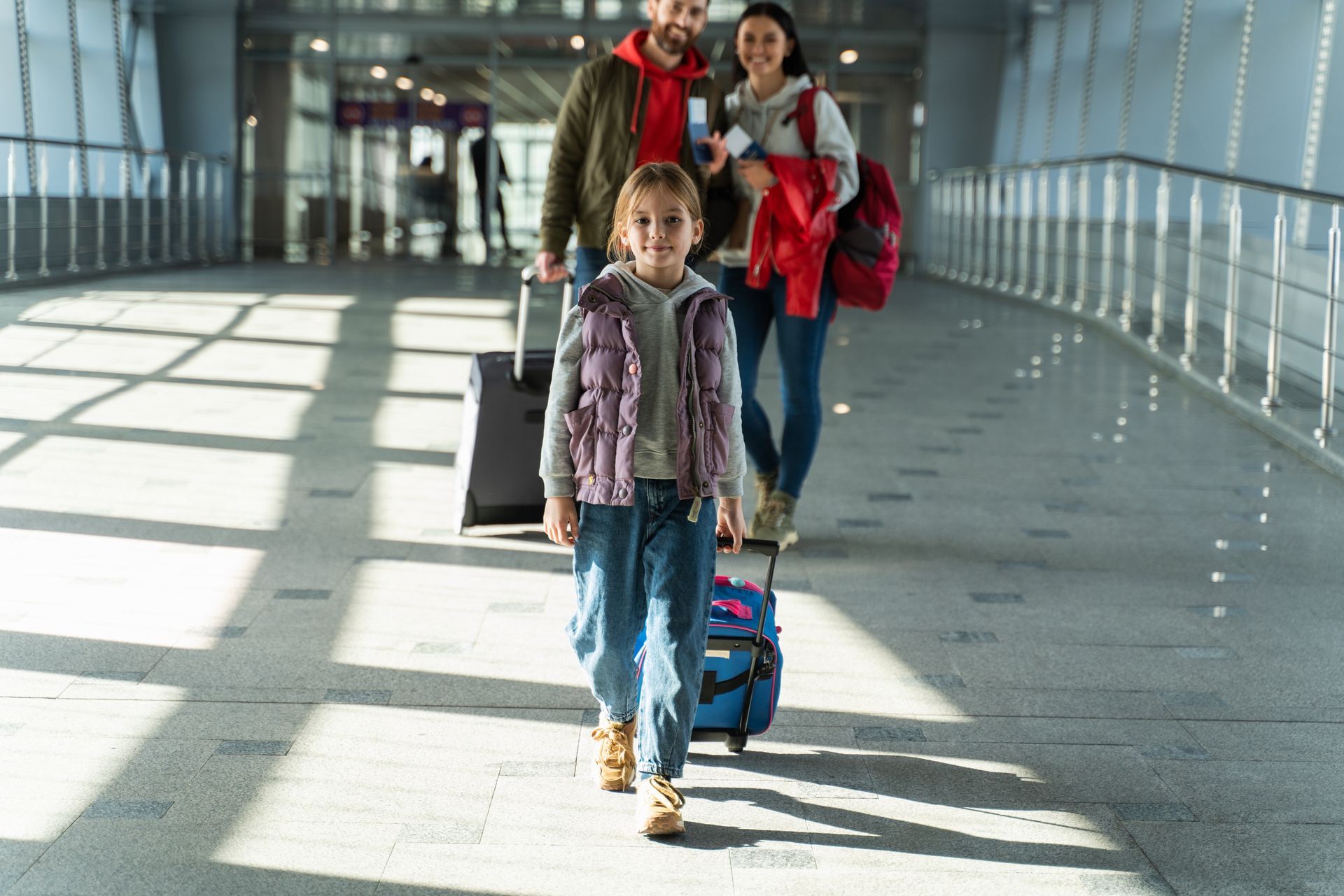 Une famille avec des bagages traverse un couloir d'aéroport. La jeune fille, souriante, ouvre la marche.