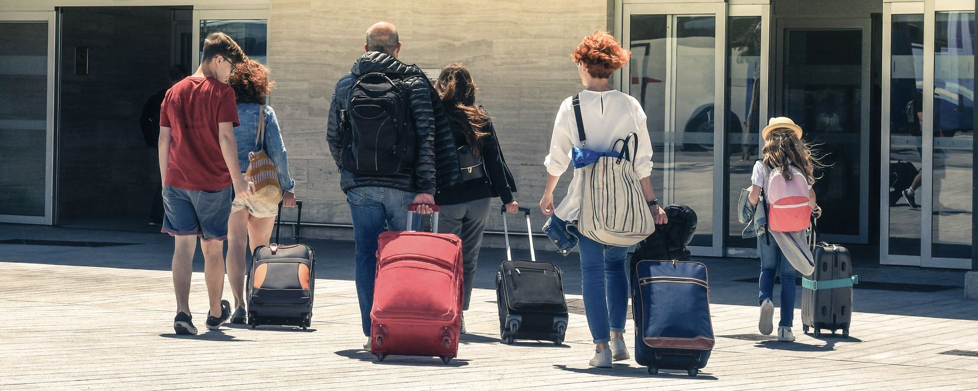 Un groupe de personnes avec des bagages se dirigeant vers un bâtiment par une journée ensoleillée.