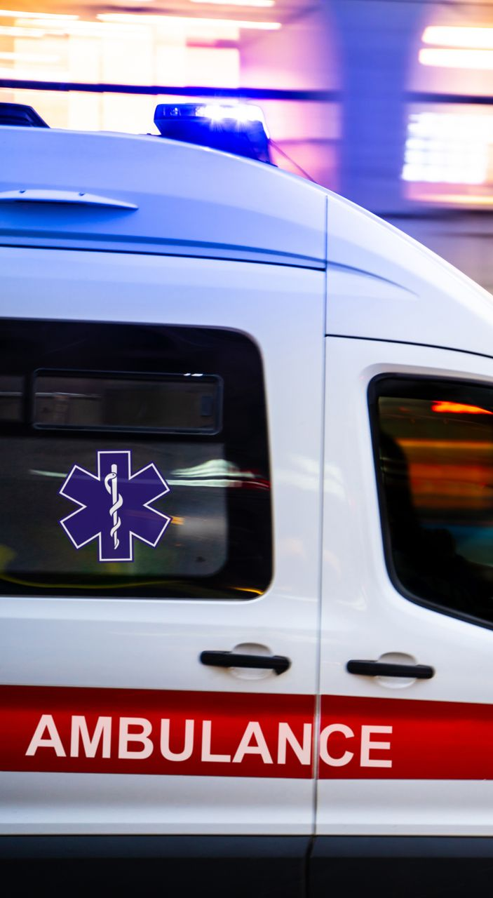 Ambulance blanche avec une bande rouge et des gyrophares bleus, roulant à vive allure.