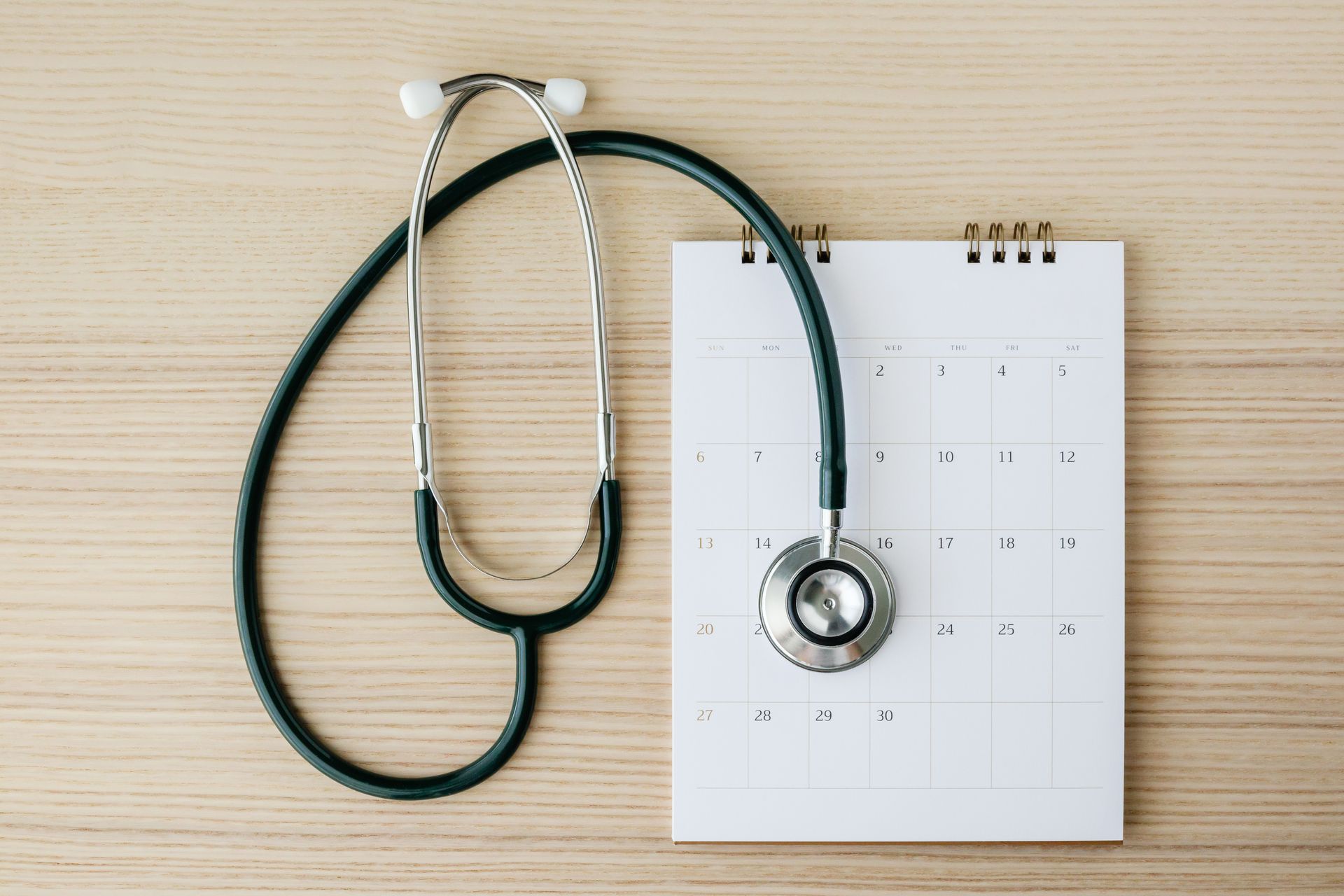 Un stéthoscope posé sur un calendrier vierge, lui-même posé sur une surface en bois.