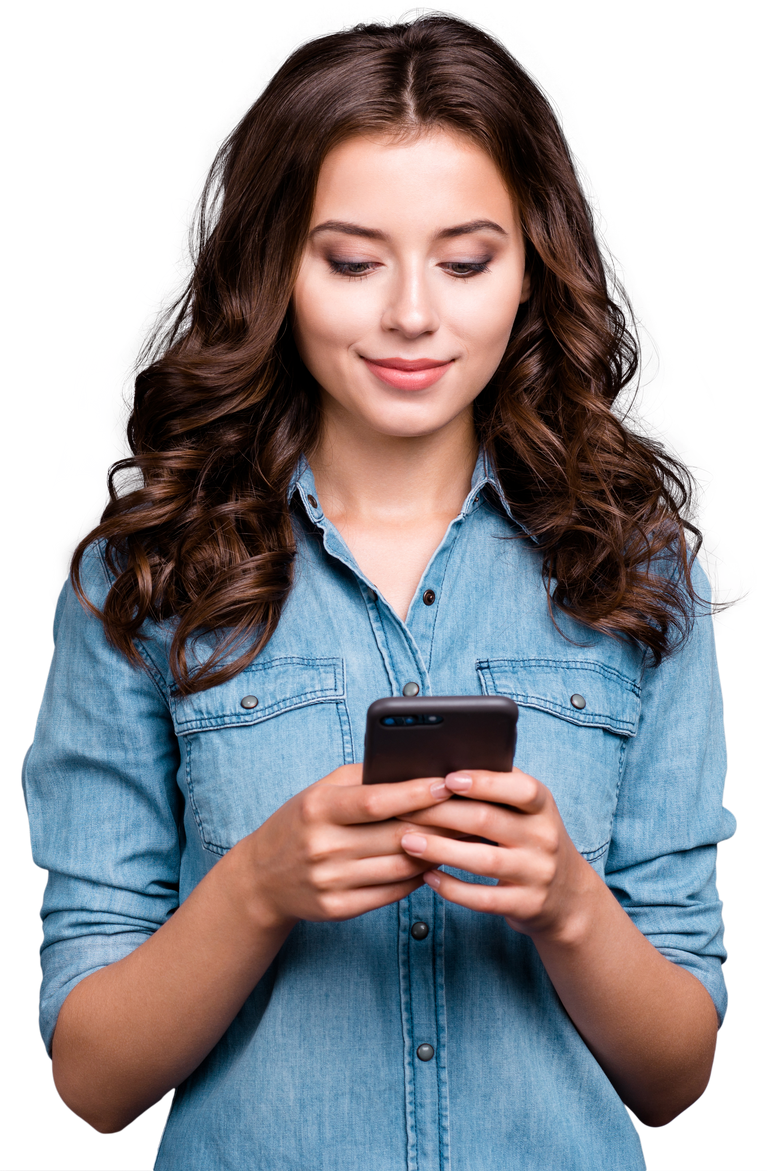 Une femme aux cheveux bruns bouclés regarde son smartphone en souriant. Elle porte une chemise en jean bleu.