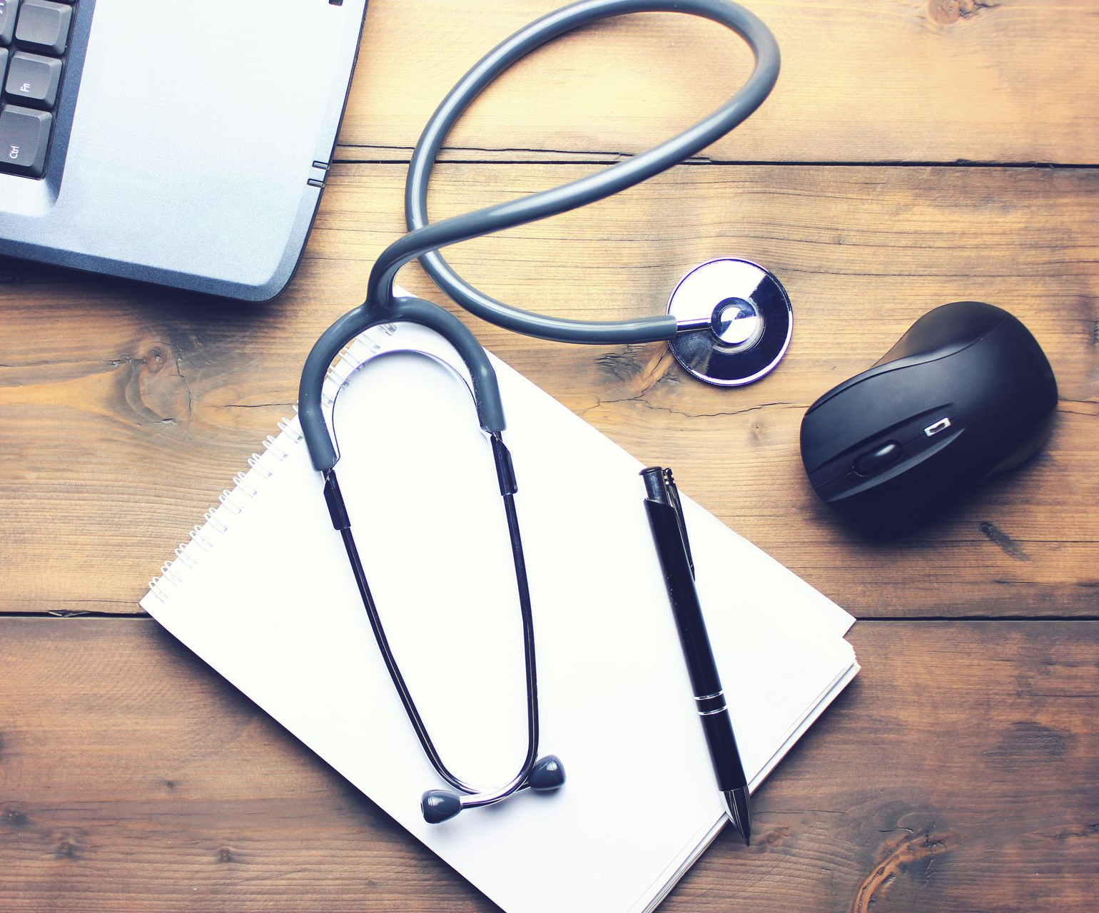 Stéthoscope, ordinateur portable, bloc-notes et souris sur un bureau en bois.