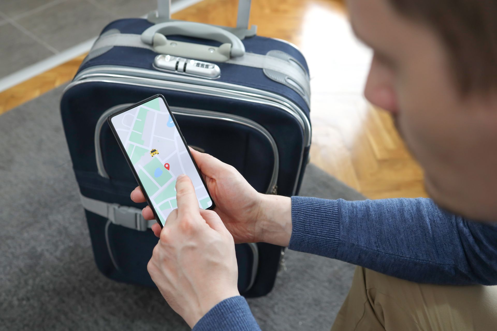 Une personne utilisant un smartphone avec une application de géolocalisation, près d'une valise.