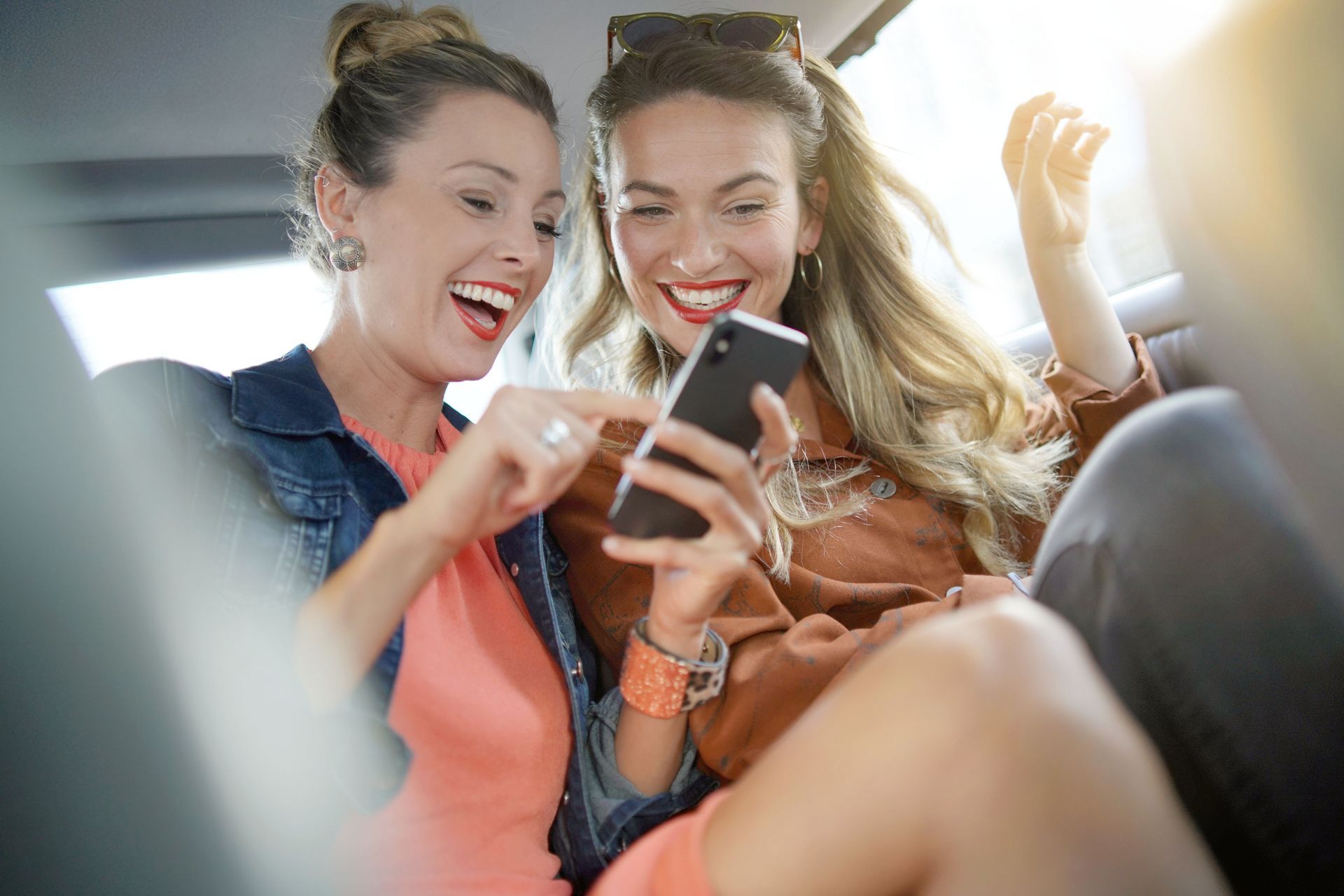 Deux femmes sourient, les yeux rivés sur leur téléphone portable dans une voiture.