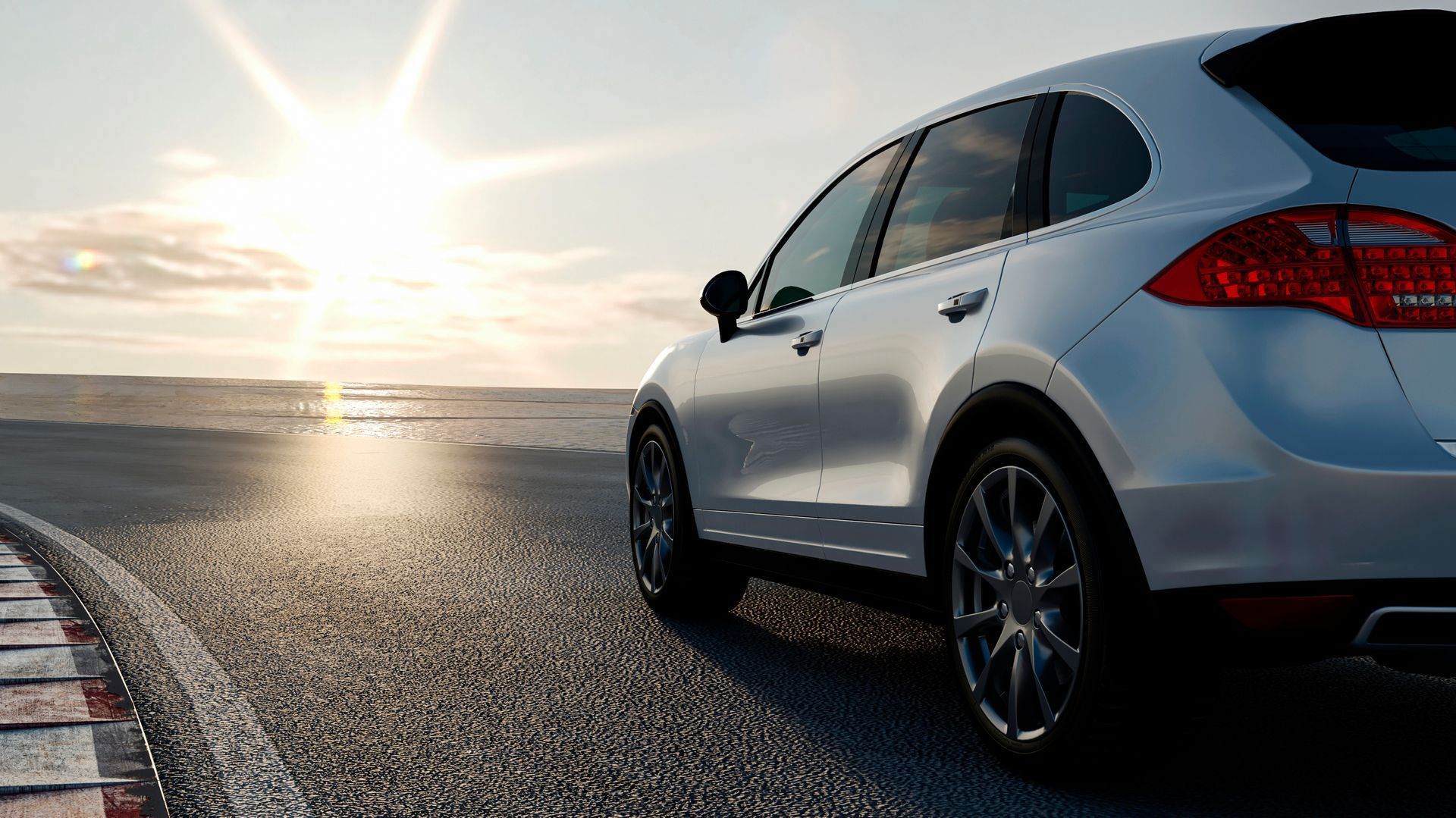 Un SUV blanc garé sur une route, le soleil se couchant sur l'océan.