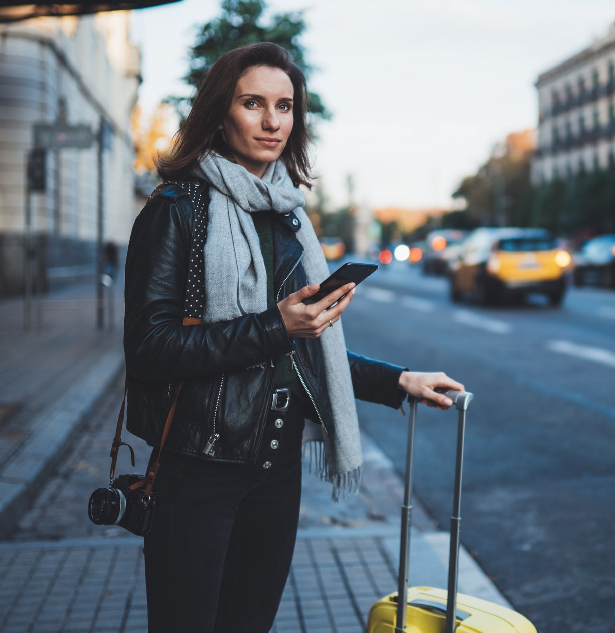 Une femme avec des bagages et un téléphone attend dans une rue en ville.