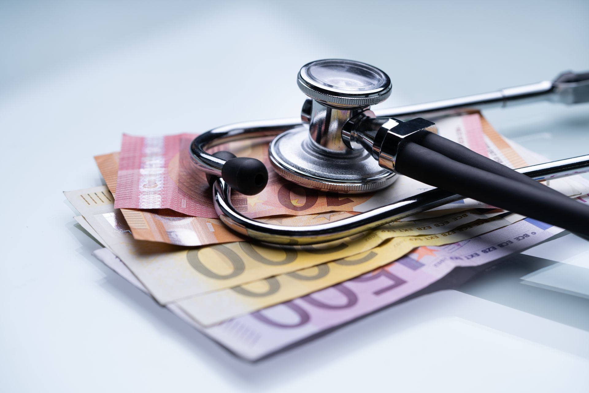 Un stéthoscope posé sur une pile de billets en euros, symbolisant le coût des soins de santé.
