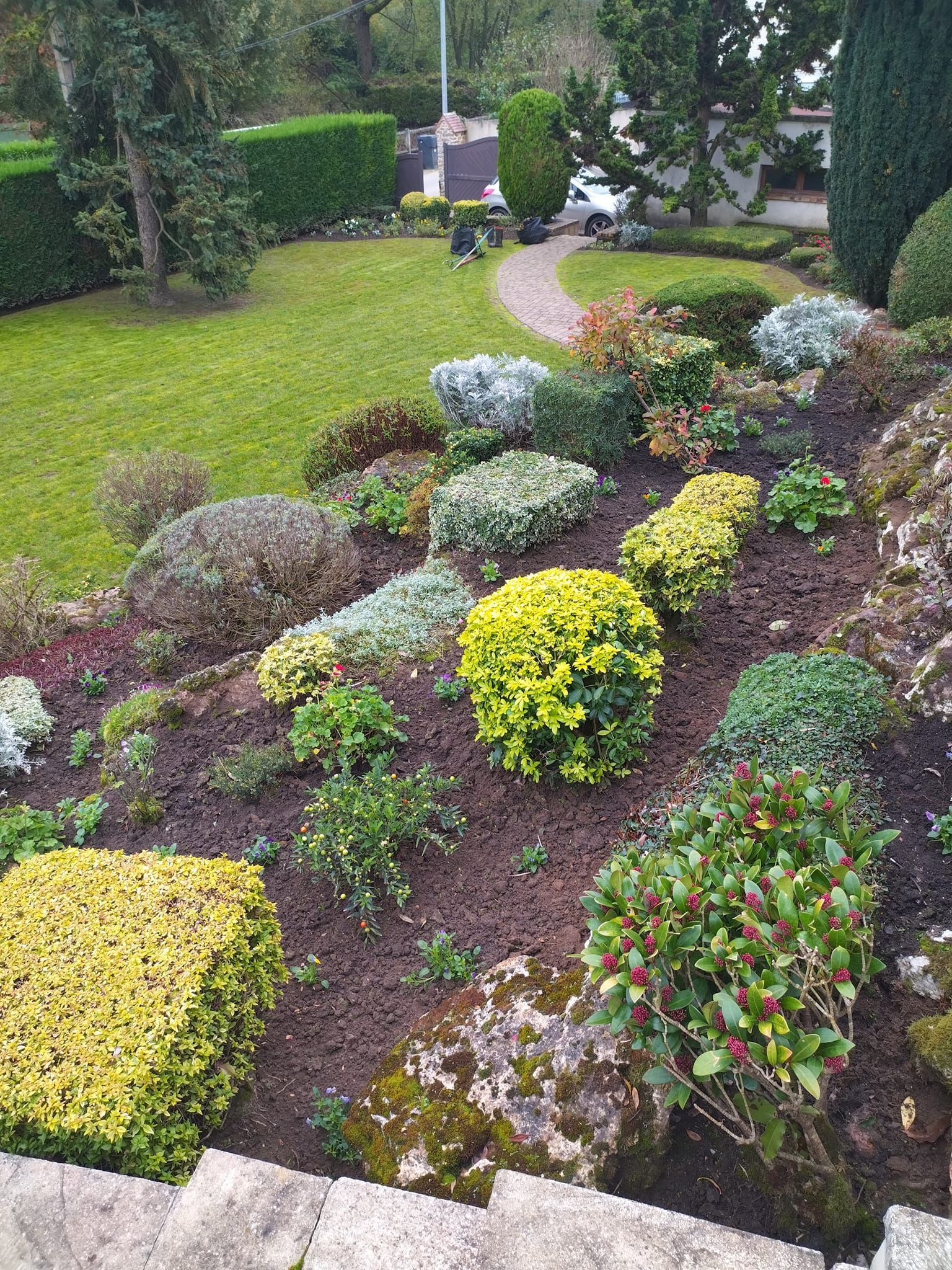 Allée de jardin sinueuse bordée d'arbustes fleuris colorés et de haies taillées avec soin dans un jardin paysager.