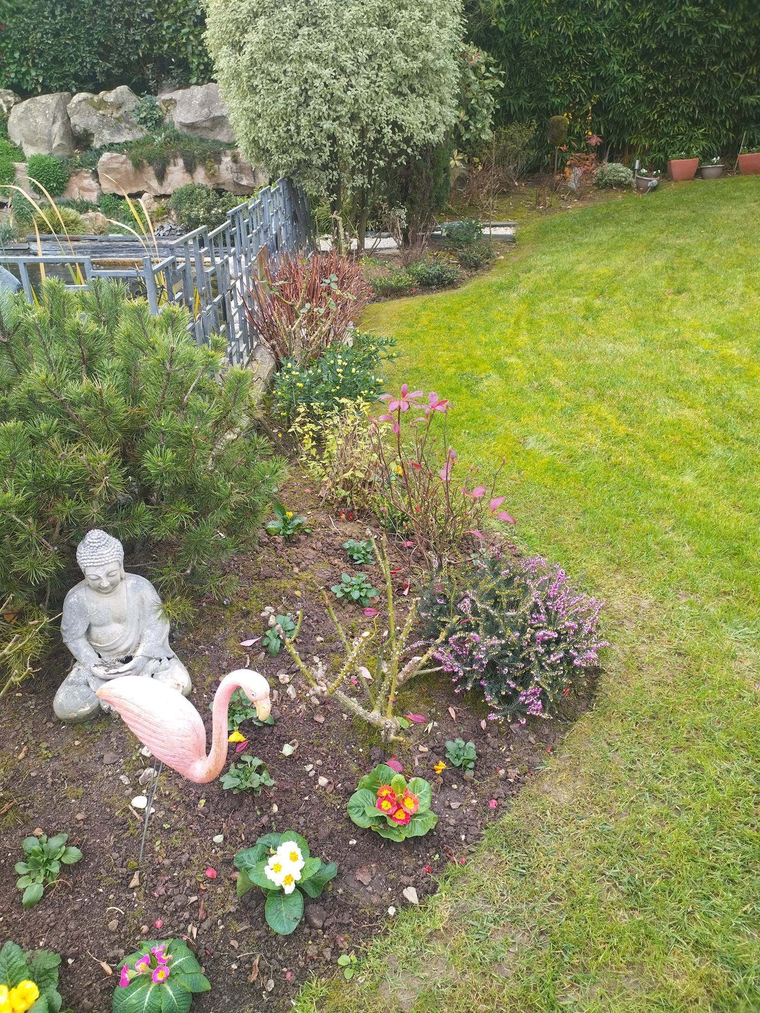 Un parterre de fleurs orné d'une statue de cygne blanc, d'une petite figurine de Bouddha et de fleurs colorées, bordant une pelouse.