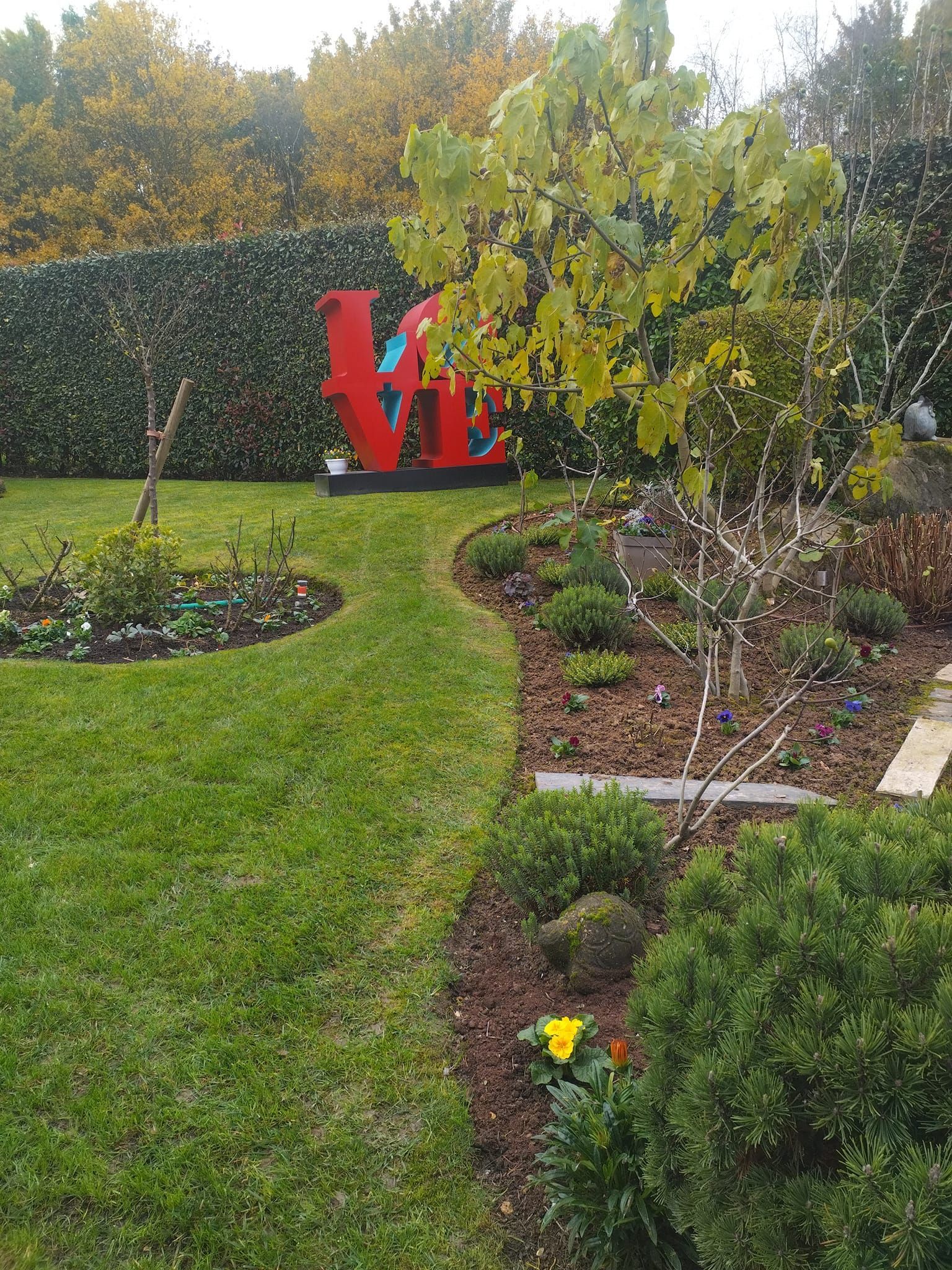 Un jardin avec un panneau rouge, une pelouse verte et des arbustes à côté d'un parterre de fleurs paillé.