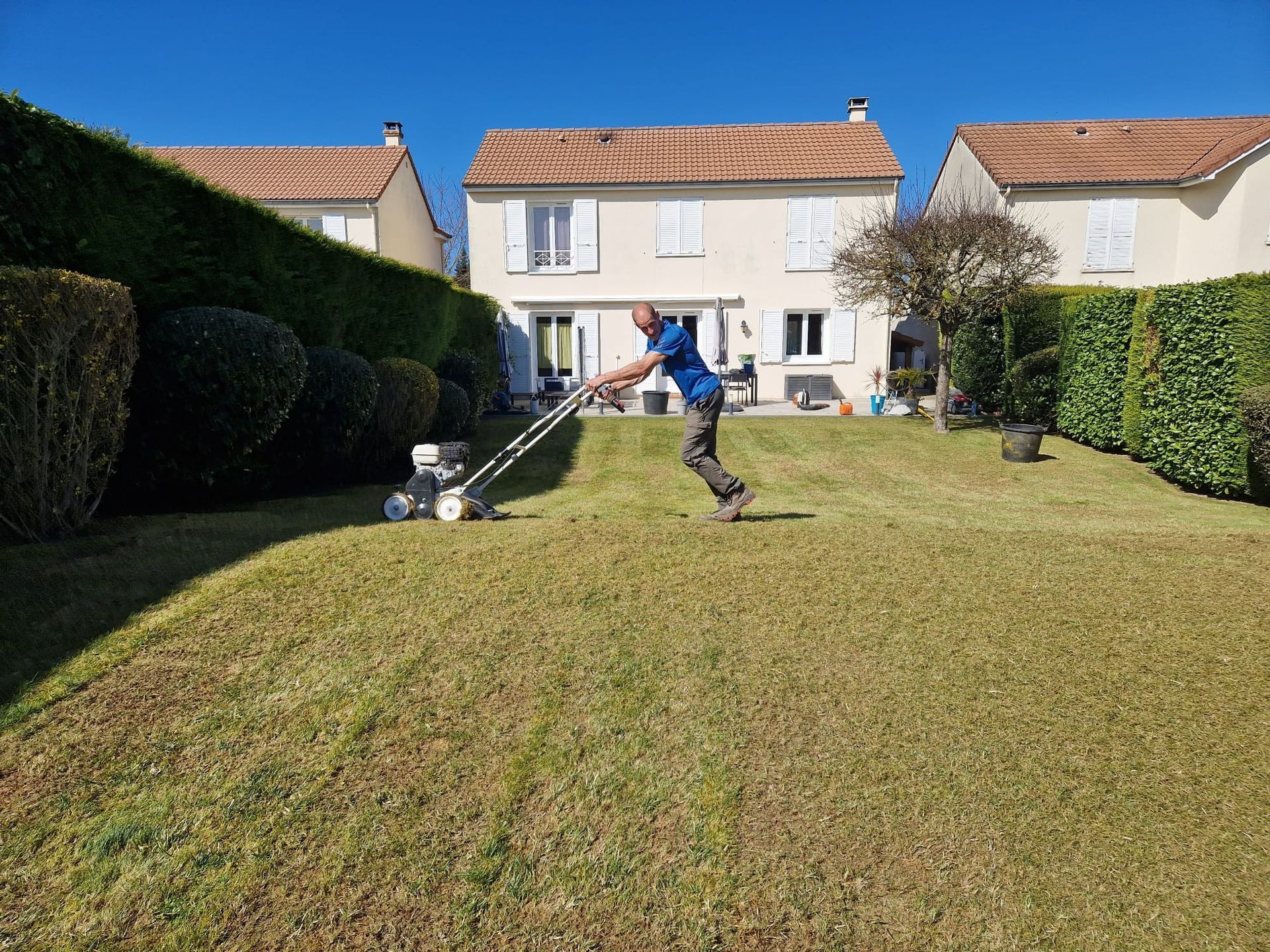 Une personne tond la pelouse d'une maison avec une tondeuse manuelle.
