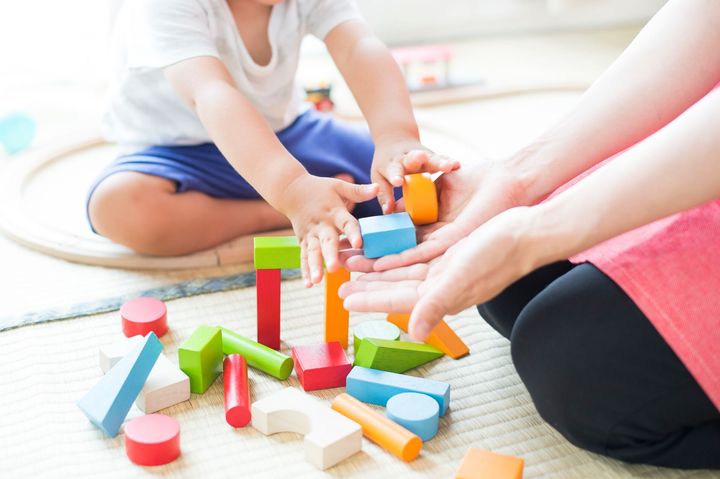Une femme et un enfant jouent avec des blocs de bois sur le sol.