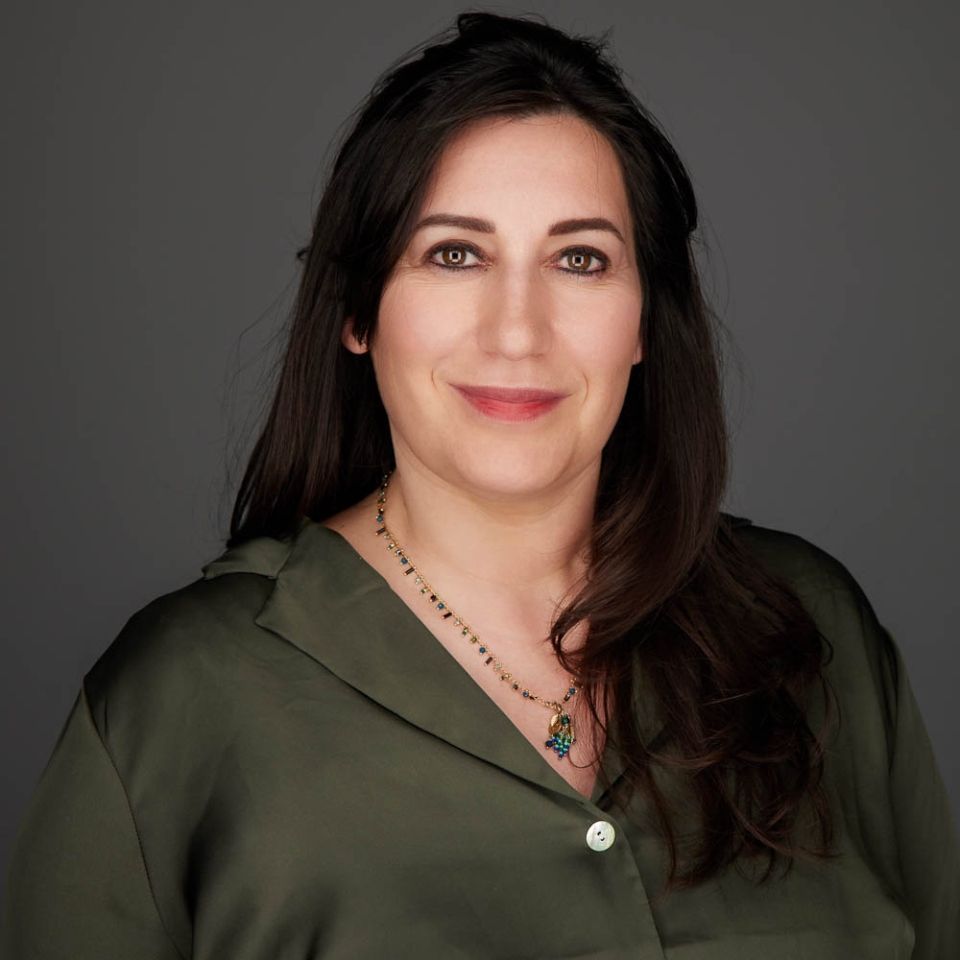 Une femme portant une chemise verte et un collier sourit à la caméra.