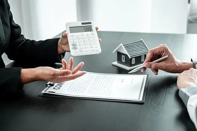 Una mujer sostiene una calculadora al lado de una casa modelo.