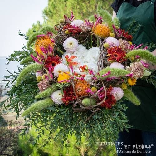 Grande couronne florale colorée avec un centre blanc, des fleurs roses et orange, et de la verdure en extérieur