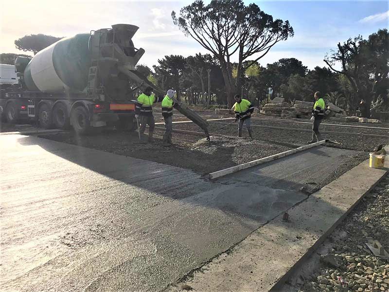 Obreros de la construcción vertiendo concreto desde un camión mezclador hacia la carretera en una intersección de calles.