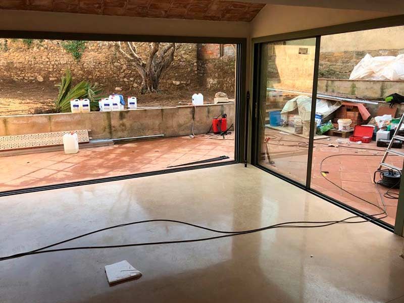 Habitación interior vacía con grandes puertas corredizas de vidrio que dan a un patio desordenado.