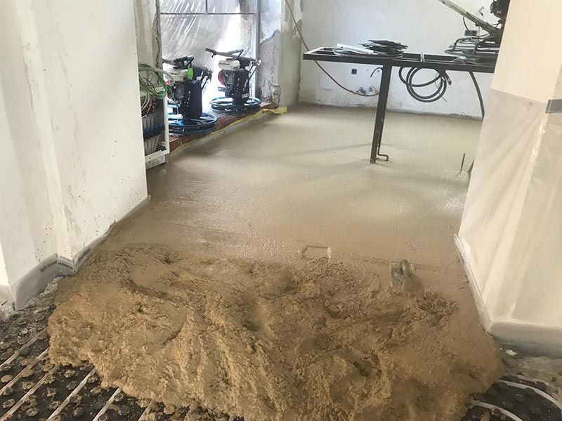 Una habitación en construcción con suelo de hormigón irregular, tierra a la vista y herramientas cerca de la pared del fondo.