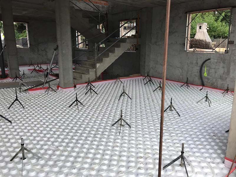 Habitación vacía de hormigón con puntales de soporte metálicos y una escalera al fondo.