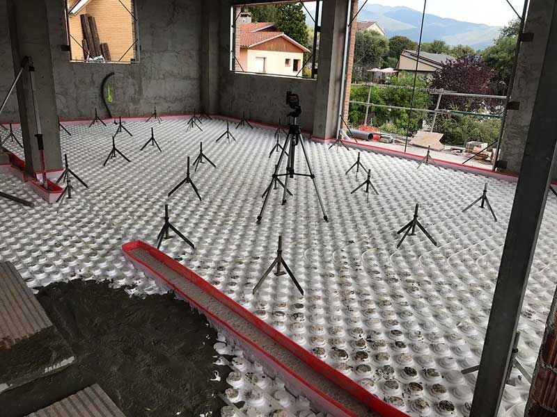 Obra en construcción con suelo de membrana blanca con hoyuelos y pilares de soporte negros bajo una estructura de techo.