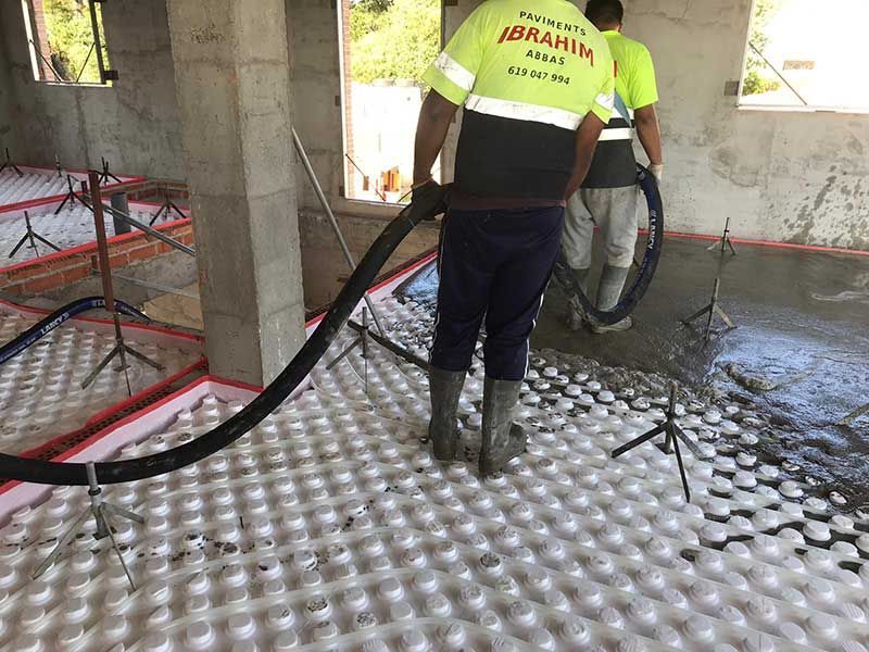 Trabajadores rociando hormigón sobre el aislamiento del suelo en una habitación sin terminar.