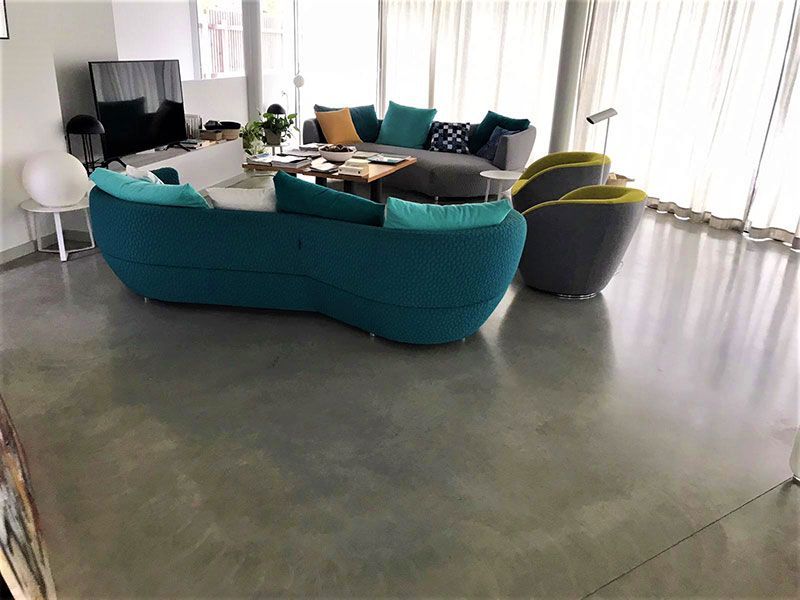 Sala de estar moderna con sofá modular color turquesa, mesa de centro redonda, televisor y grandes ventanales con cortinas.