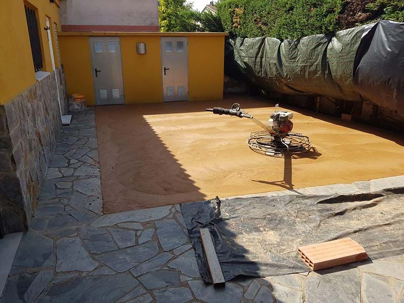 Patio de piedra con paredes y puertas amarillas, y un pequeño objeto en espiral en el suelo cerca de una valla cubierta con una lona.
