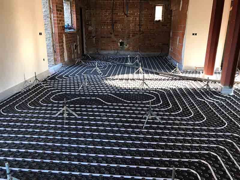 Suelo de habitación sin terminar con tuberías negras de calefacción radiante colocadas sobre el aislamiento.