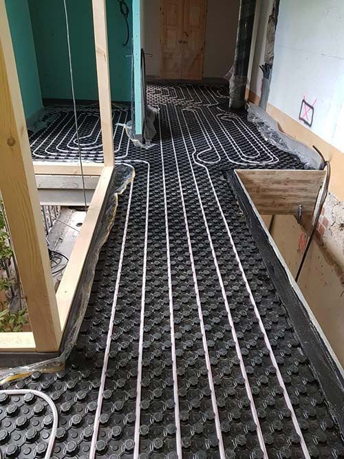 Pasillo de construcción con esteras negras de calefacción por suelo radiante y tuberías blancas instaladas en el suelo.