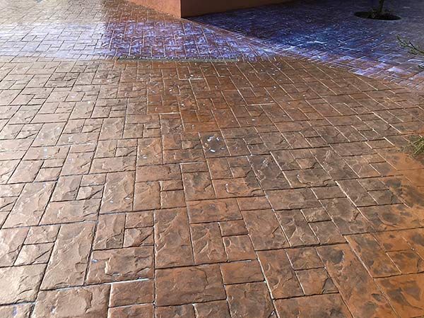 Pavimento de ladrillos mojado bajo una pasarela cubierta con un oscuro desagüe al fondo.