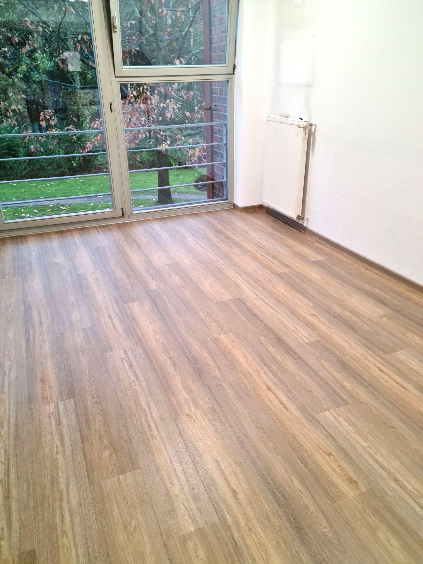 Ein leerer Raum mit Holzboden und großem Fenster.