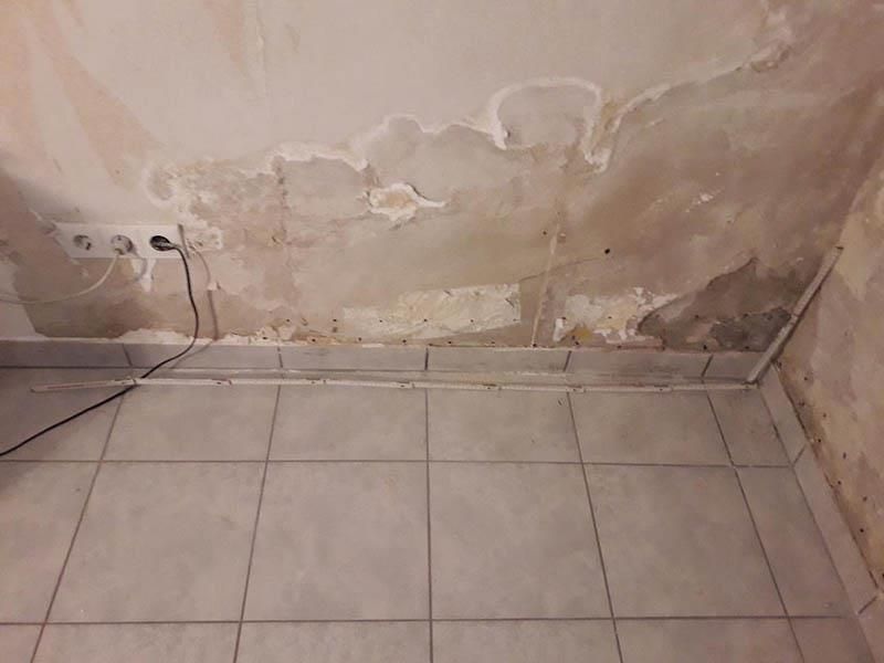 Ein Badezimmer mit gefliestem Boden und einer Wand mit abblätternder Farbe.