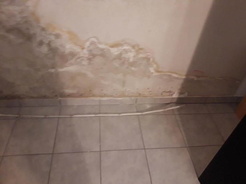 Ein Raum mit gefliestem Boden und einer Wand, deren Farbe abblättert.