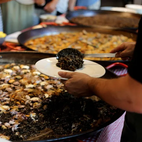 Una persona sostiene un plato de comida frente a una sartén con comida.