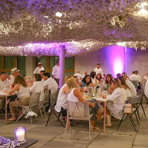 Un grupo de personas están sentadas en mesas en una habitación con flores en el techo.