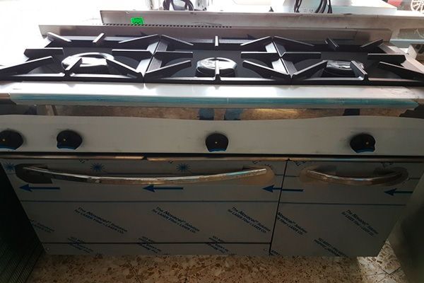 Cocina a gas comercial de acero inoxidable con cuatro quemadores y dos puertas de horno.
